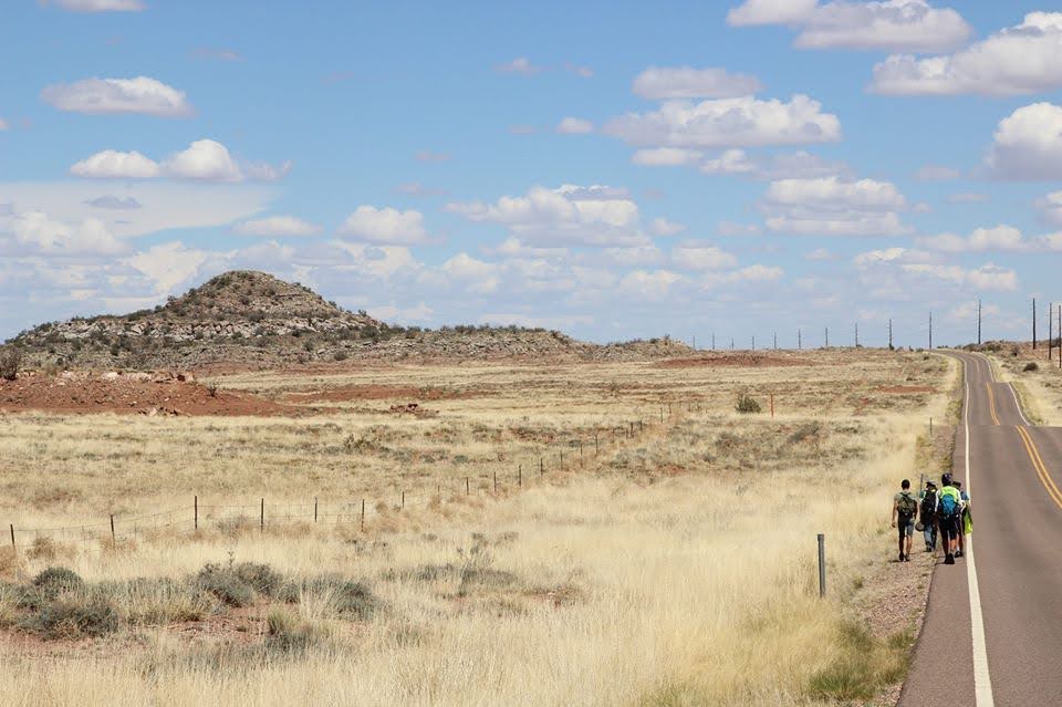 Image of desert horizon with small group of us walking along highway stretching into infinity.